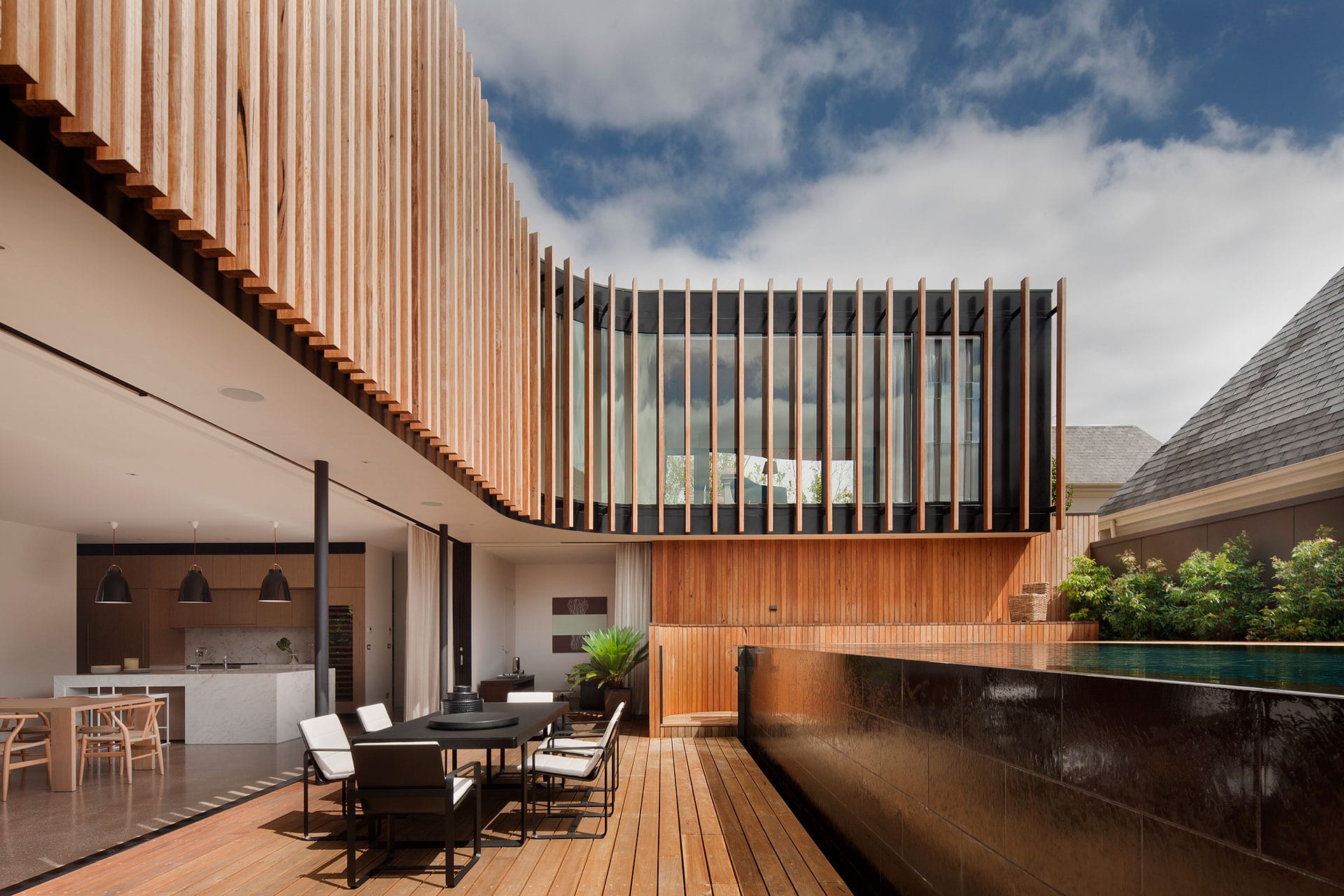 Imagen de una terraza moderna con mobiliario de exterior, muros de madera y grandes ventanales que reflejan el cielo. Ideal para diseño arquitectónico y decoración de exteriores.